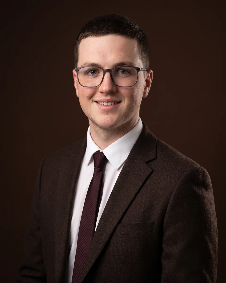 Portrait of Dylan Byrne in a brown blazer and burgundy tie